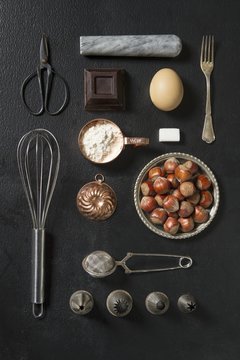 An arrangement of kitchen utensils and baking ingredients on a dark surface