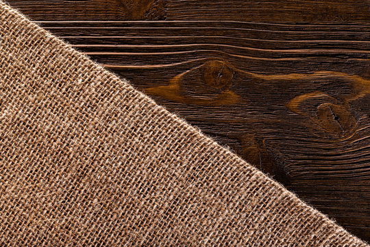Macro image of textured hessian textile at brown wooden board background divided diagonally.