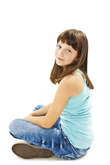 Closeup image of a pretty little girl sitting on the floor in jeans. Isolated on white background