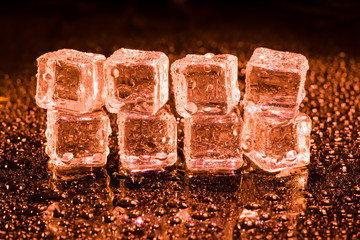 Ice cubes in red light on black wet table.
