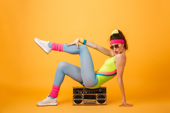 Playful young woman athlete sitting on retro boombox and posing
