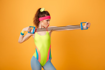 Serious focused young fitness woman standing and training with expander