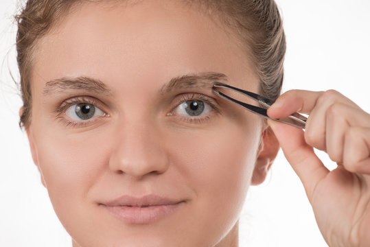 Young girl pulls out her eyebrows with tweezers metal on a white background