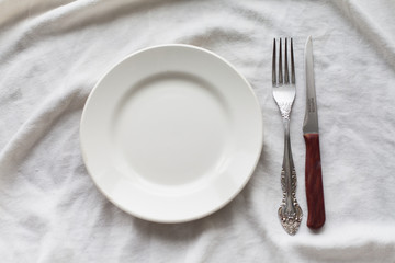 Tableware, white plate, fork, knife on a white tablecloth