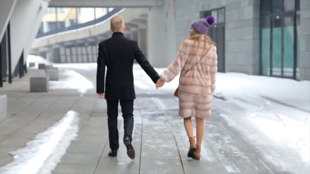 Happy woman and man couple walking together in the city holding hands together. Relationship concept. Woman wearing fur coat.