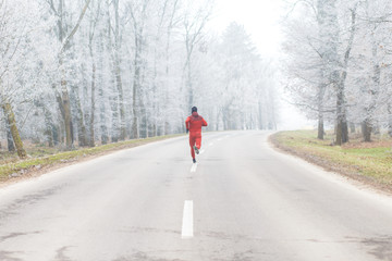 Back view of young athletic man running on the road in winter.