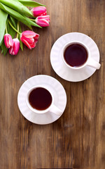 Pink tulips on wooden background, two cups of tea and coffee on saucers with hearts marmalade