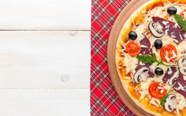 fresh pizza in a rustic Italian style with jerky olives mushrooms and three kinds of cheese on a light wooden background