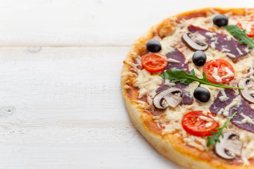 fresh pizza in a rustic Italian style with jerky olives mushrooms and three kinds of cheese on a light wooden background