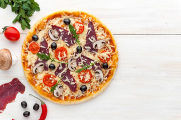 fresh pizza in a rustic Italian style with jerky olives mushrooms and three kinds of cheese on a light wooden background