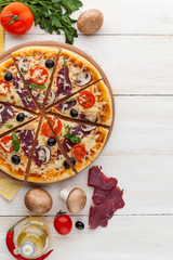 fresh pizza in a rustic Italian style with jerky olives mushrooms and three kinds of cheese on a light wooden background