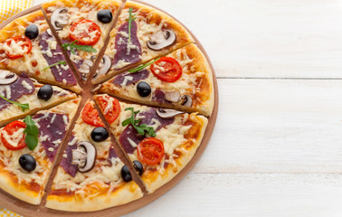 fresh pizza in a rustic Italian style with jerky olives mushrooms and three kinds of cheese on a light wooden background
