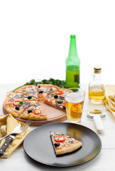 fresh pizza in a rustic Italian style with jerky olives mushrooms and three kinds of cheese on a light wooden background with a bottle of cold beer