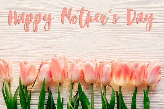 happy mother's day text sign on pink tulips on white rustic wooden background. greeting card concept. sensual tender women image. spring flowers flat lay