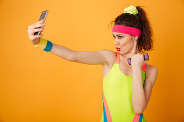 Happy playful young woman athlete holding dumbbell and taking selfie