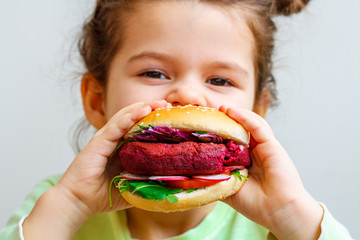 Happy hungry child (girl) eating healthy vegan burger.