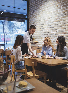 Waiter serving coffee to three pretty women at coffee shop.