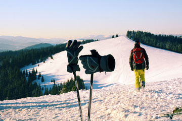 Ski poles and gloves and skier that goes uphill on the background of the Carpathian Mountains