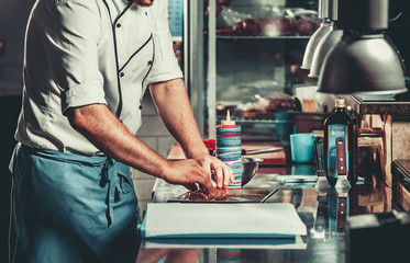 Young white chef in kitchen interior. Man marinating beef steak on a tray. Meat ready for the grill and serve. Only hands