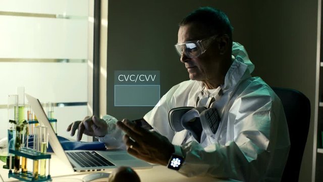 Middle aged senior scientist or chemist in protective clothes enter CVC or CVV code while e-shopping and pay online. Shot can be used to demonstrate process of secure e-commerce by professional buyers