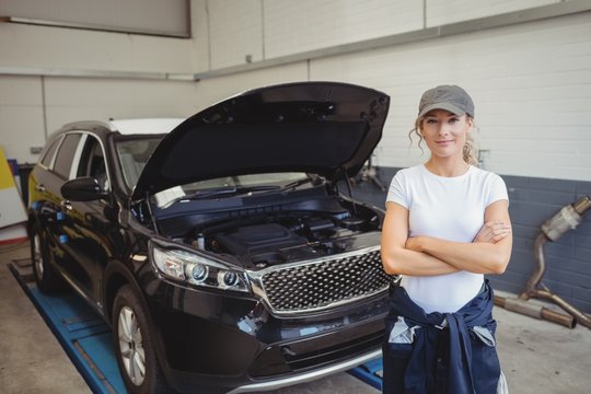 Female mechanic standing with arms crossed in front of car