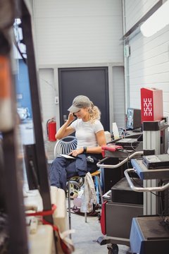 Female mechanic using digital tablet while talking on mobile phone in repair garage
