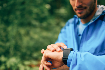 Fit male jogger day using a smartwatch during cross country forest trail race in a nature park.