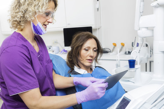 Assistant Showing Report To Patient On Digital Tablet In Dentist