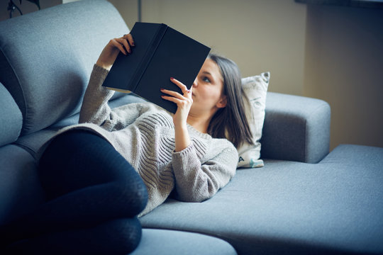 Ragazza legge libro sul divano a casa