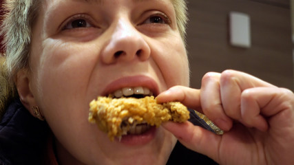 Woman expressively eats chicken in fast food restaurant. Face closeup shot.