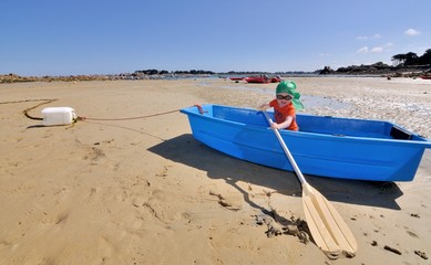 Fototapeta na wymiar Un petit garçon joue avec une rame dans une barque à marée basse en Bretagne