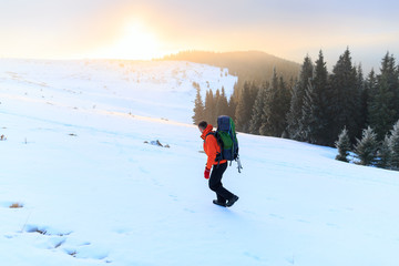Fototapeta na wymiar Hiker in winter mountains. Man with backpack trekking in mountains. Winter hiking. Beautiful sunrise in the winter mountains.