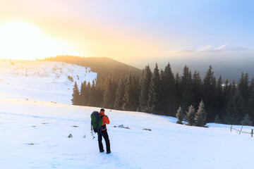 Hiker in winter mountains. Man with backpack trekking in mountains. Winter hiking. Beautiful sunrise in the winter mountains.
