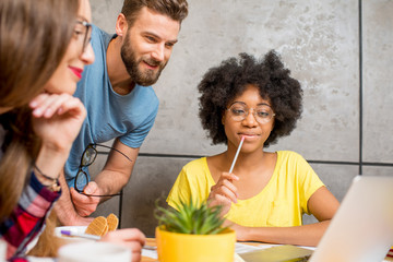 Multi ethnic coworkers dressed casually in colorful clothes talking together sitting with laptop...
