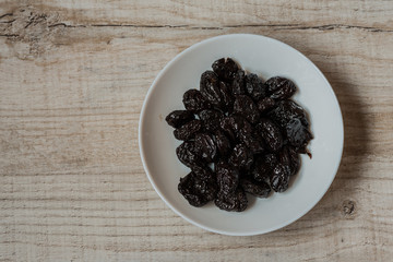 prunes in a bowl on a light wooden background