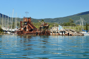 Seen from the sea sunken by the coast of Lefkada Island, Greece old ruined boats and a rusty dredge