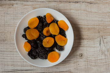 prunes and dried apricots in a bowl on a light wooden background