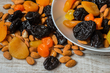 prunes, dried apricots, dried mandarins and almonds in a bowl on a light wooden background