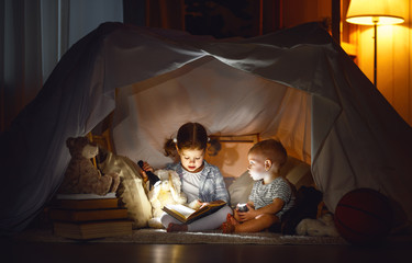 Fototapeta na wymiar children boy and girl reading book with flashlight in tent