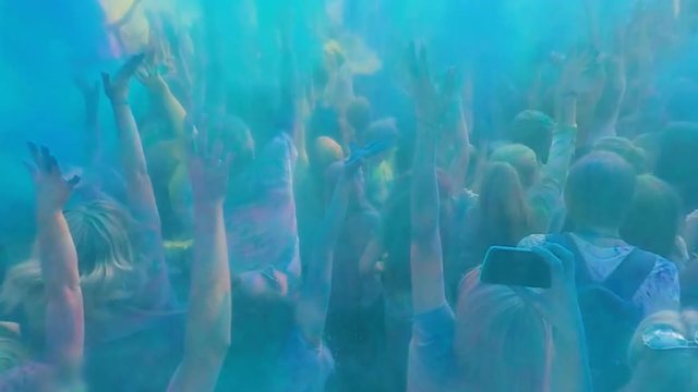 Happy crowd of young people throwing blue powder in air, enjoying paint festival