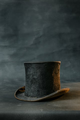 Worn damaged old and vintage black top hat isolated against dark background