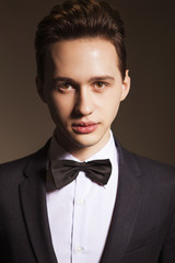 Young handsome brunette macho businessman in black suit and bow tie. neutral background