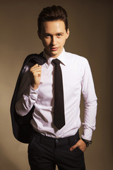 Young handsome brunette macho businessman in black suit and tie. neutral background