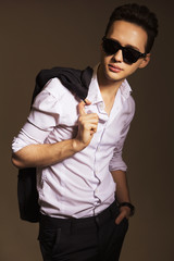 Young handsome brunette macho businessman in black suit and white shirt in sunglassess. neutral background