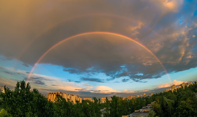 Evening rainbow in the sky over the city at sunset in the summer, in the rain
