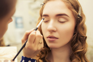 Brunette make up artist woman applying make up for a blonde bride in her wedding day, for a date