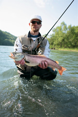 Huchen / Fisherman standing in deep water presenting caught Danube salmon. Spin fishing in San River, Sub-Carpathian region. The huchen occurs also in Danajec River.
