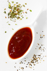 Tomato paste on small spoon with dried oregano and ground black pepper on the side, photographed overhead on white wood with natural light (Selective Focus, Focus on the top of the paste)