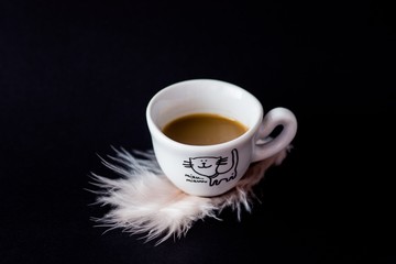 kawa w małej filiżance z piórkiem na ciemnym tle