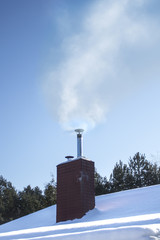 Zaśnieżony dach z kominem z którego wydobywa się dym. Zanieczyszczenie powietrza z gospodarstw domowych. - obrazy, fototapety, plakaty